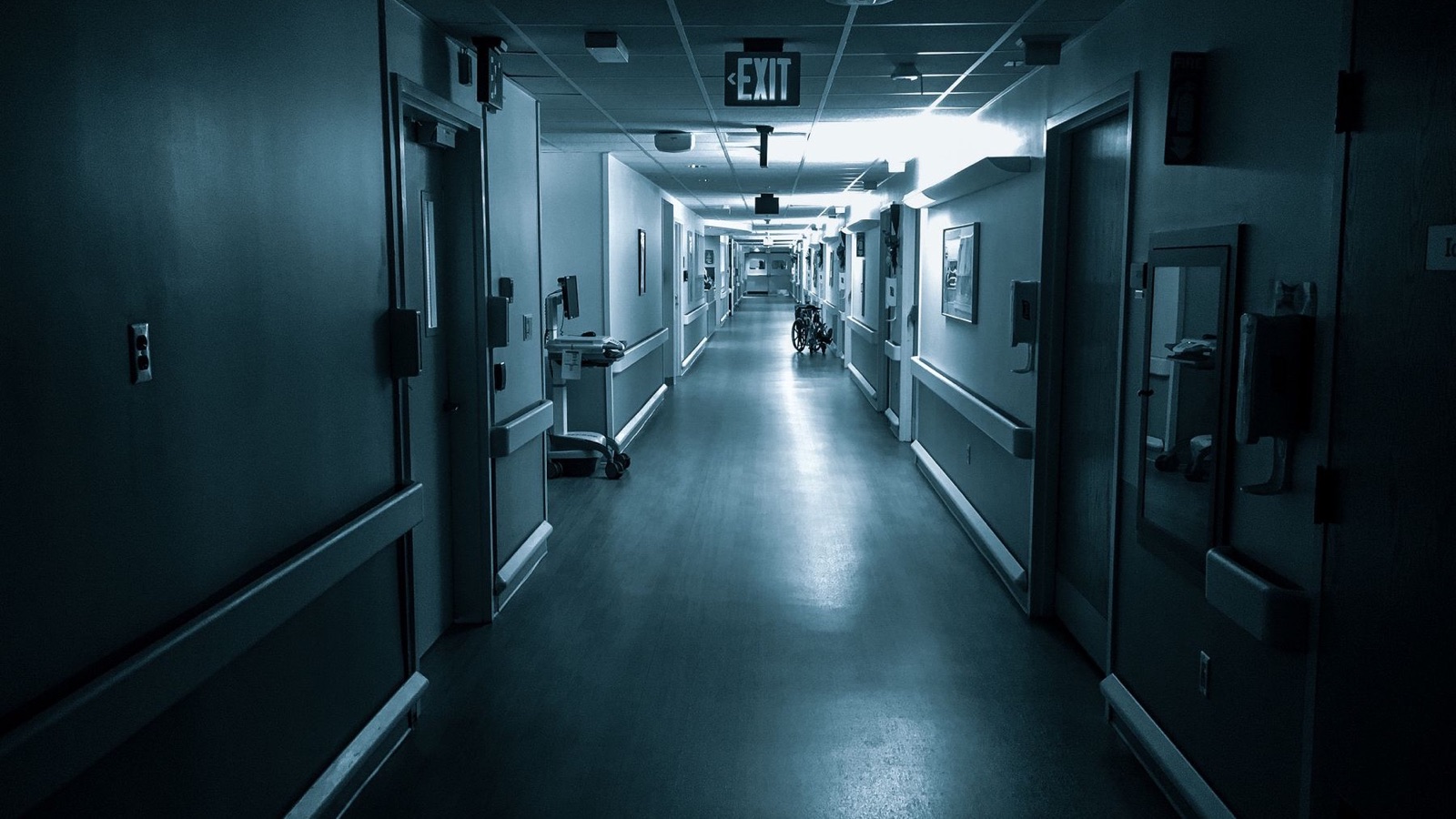 Corridoio d'ospedale poco illuminato con una sedia a rotelle in lontananza